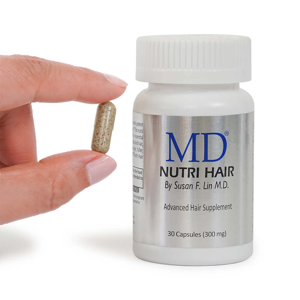 Hand holding small MD Nutri Hair capsule next to bottle – daily supplement for thinning hair and drug-free hair loss support