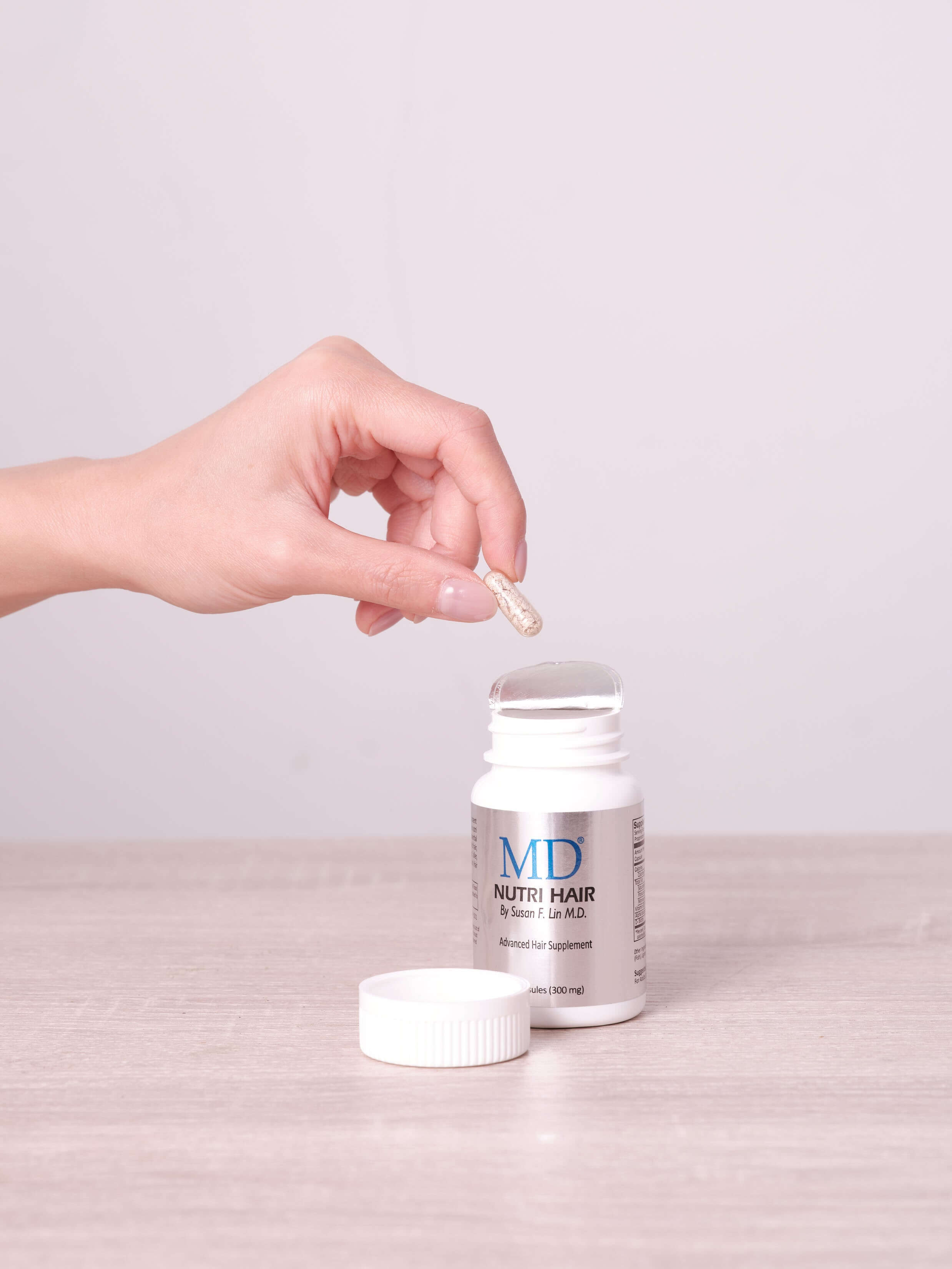 Hand removing a small, easy-to-swallow capsule from MD Nutri Hair bottle, showing actual capsule size – natural hair growth supplement from MD Hair with plant-based ingredients
